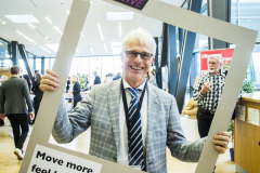 Person im Anzug hält einen großen Rahmen mit den Aufschriften „#BEACTIVE“ und „Move more, feel better.“
