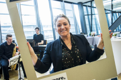 Frau hält einen großen Rahmen mit Aufschrift „#BEACTIVE“ und „Move more, feel better.“ in einem hellen Raum.
