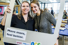 Zwei Frauen stehen in einem großen weißen Fotorahmen mit den Aufschriften „#BEACTIVE“ und „Move more, feel better.“
