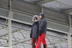Zwei Personen in Winterkleidung und Helmen stehen unter einem Metalldach.