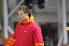 Person in rotem Shirt und orangefarbener Jacke, Kopf seitlich, Gesicht verpixelt.