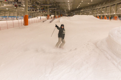 Person beim Skifahren in einer überdachten Schneehalle, mit Helm und Skistöcken.