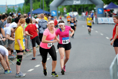 Zwei Läuferinnen in pinken Shirts mit Startnummern 16-2 und 16-1 laufen auf einer Straße ins Ziel.