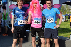 Drei Personen mit Startnummern, pinken Flügeln und farbigen Sportshirts stehen nebeneinander im Freien.