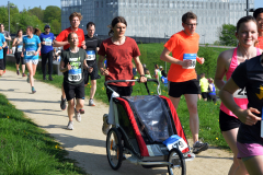 Mehrere Läufer auf einem Weg; vorne ein Kinderwagen zum Joggen, im Hintergrund ein Gebäude.