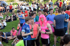 Viele Menschen stehen und sitzen auf einer Wiese; mehrere tragen bunte Sportkleidung und Kostüme.