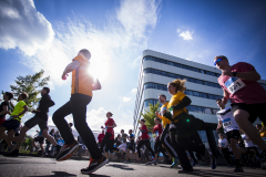 Läufergruppe auf einer Straße vor einem Bürogebäude bei sonnigem Himmel, im Vordergrund mehrere Personen im Lauf.