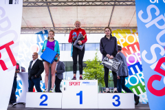 Drei Sportlerinnen auf einem Siegerpodest mit den Plätzen 1, 2 und 3, jede hält eine Urkunde oder Tasche.