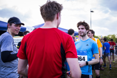 Läufer stehen im Freien an einem Startbereich; vorn ein Mann in rotem Shirt, rechts ein Mann mit Startnummer 964.