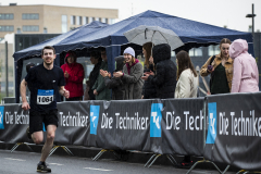 Läufer mit Startnummer 1064 läuft im Regen an Zuschauern unter Zelten und einem Schirm vorbei.