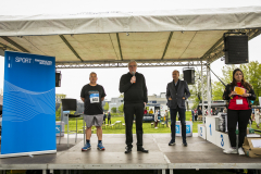 Vier Personen auf einer Bühne unter einem Zeltdach, links ein blaues RWTH-Aachen-Sportbanner, rechts ein Siegerpodest.