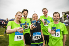 Fünf Personen in grünen Shirts stehen draußen und halten Becher mit der Aufschrift „KOMM INS TEAM 10!“.