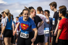 Läuferin im blauen Superman-T-Shirt mit Startnummer 83-2, umgeben von weiteren Läufern im Freien.