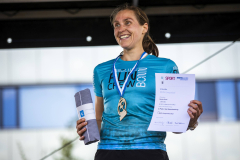 Frau im blauen Laufshirt mit Medaille, Urkunde und zusammengerollter Broschüre in den Händen.