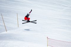 Skifahrerin springt auf einer verschneiten Piste über eine Schanze.