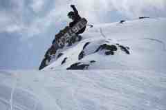 Snowboarder springt in der Luft vor einer verschneiten Felswand.