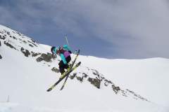 Skifahrer springt mit Skiern über eine verschneite Bergflanke.