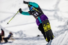 Skifahrer springt mit ausgestreckten Stöcken über eine Schneekante.