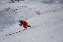 Skifahrer in orangefarbener Ausrüstung fährt eine steile, verschneite Piste hinab.
