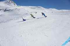 Zwei Snowboarder fahren eine präparierte Piste im verschneiten Gebirge hinunter.