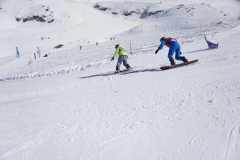 Zwei Snowboarder fahren eine verschneite Skipiste hinunter.
