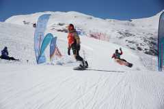 Snowboarder auf einer sonnigen Skipiste mit verschneiten Bergen im Hintergrund.