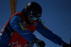 Snowboarder in Schutzkleidung mit Helm beugt sich vor, vor blauem Himmel.