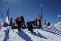 Snowboarder starten bei einem Wettkampf von einer verschneiten Rampe im Gebirge.