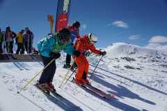 Skifahrer starten ein Rennen auf einer verschneiten Bergpiste bei sonnigem Wetter.