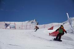 Snowboarder fahren einen präparierten Hang im Slalom unter blauem Himmel hinab.