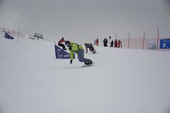 Snowboarder fahren bei einem Rennen einen verschneiten Hang hinab.