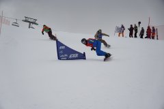 Snowboarder im Rennen auf einer verschneiten Piste mit Zuschauern am Rand.