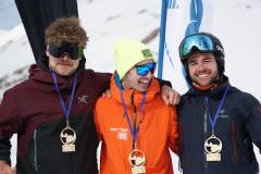 Drei Snowboarder mit Medaillen posieren gemeinsam vor verschneitem Bergpanorama.
