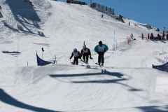 Drei Skifahrer springen gemeinsam über eine Kuppe auf einer präparierten Skipiste.