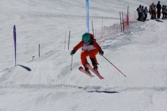 Skifahrer in roter Ausrüstung springt über eine Schneepiste.
