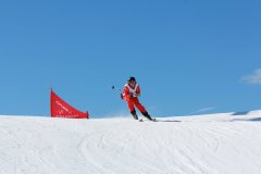 Skifahrer in roter Rennkleidung fährt eine verschneite Piste hinab.