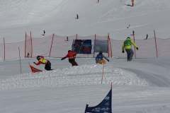 Mehrere Snowboarder fahren auf einer präparierten Skipiste zwischen Sicherheitsnetzen und Torstangen bergab.
