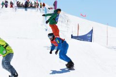 Snowboarder auf einer sonnigen Piste bei einem Rennen mit mehreren Fahrern.