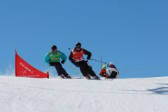Zwei Skifahrer im Rennen auf einer verschneiten Piste vor blauem Himmel.