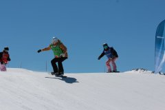 Snowboarder fahren eine schneebedeckte Piste bei klarem, blauem Himmel hinunter.