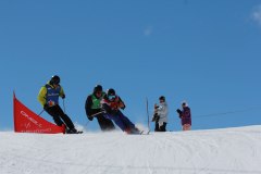 Mehrere Skifahrer fahren einen verschneiten Hang hinunter, während Zuschauer am Pistenrand zusehen.