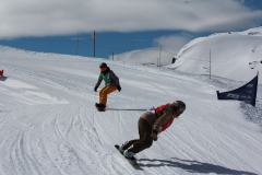 Zwei Snowboarder fahren auf einer verschneiten Piste einen Hang hinunter.