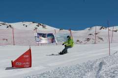 Snowboarder in grüner Jacke fährt auf einer präparierten Piste an roten Absperrnetzen vorbei.