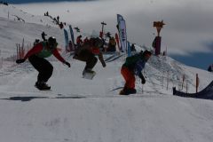 Snowboarder in der Luft bei einem Rennen auf einer verschneiten Piste.