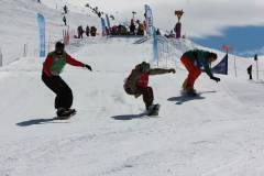 Drei Snowboarder fahren einen steilen, präparierten Hang hinunter.
