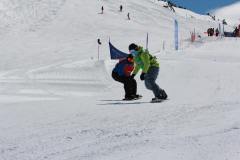 Zwei Snowboarder auf einer präparierten Skipiste fahren dicht nebeneinander.