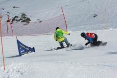 Zwei Snowboarder fahren auf einer präparierten Piste durch einen Slalomkurs im Schnee.