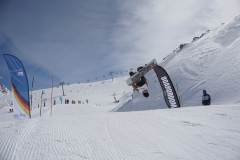 Snowboarder macht einen Backflip über einer schneebedeckten Piste im Skigebiet.