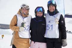Drei Snowboarderinnen oder Snowboarder mit Medaillen posieren im Schnee bei einer Siegerehrung.
