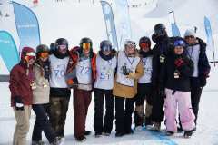 Gruppe von Snowboardern mit Startnummern und Medaillen bei einem Winterwettbewerb im Schnee.